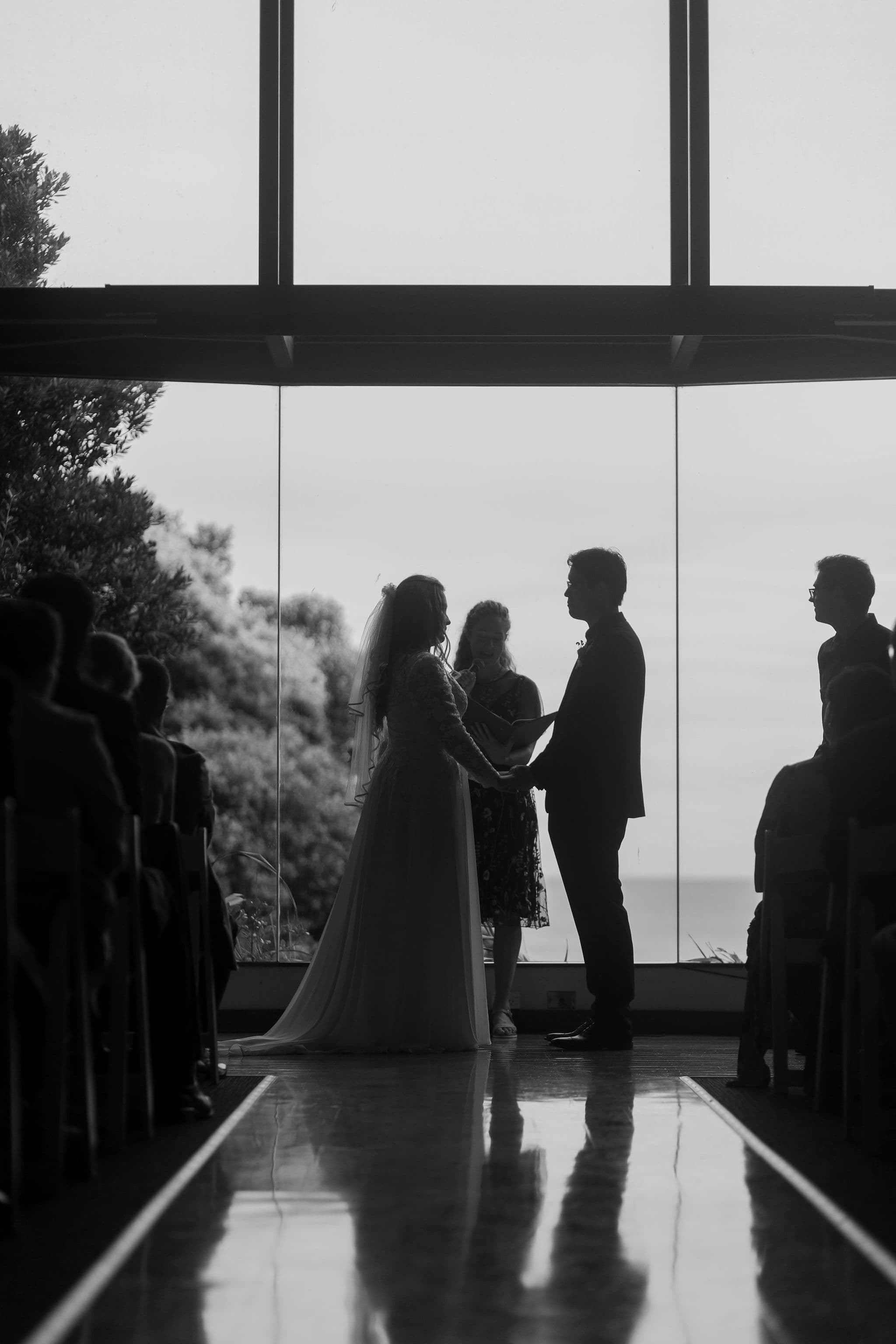 A couple stands at the altar during a wedding ceremony, holding hands, in silhouette.